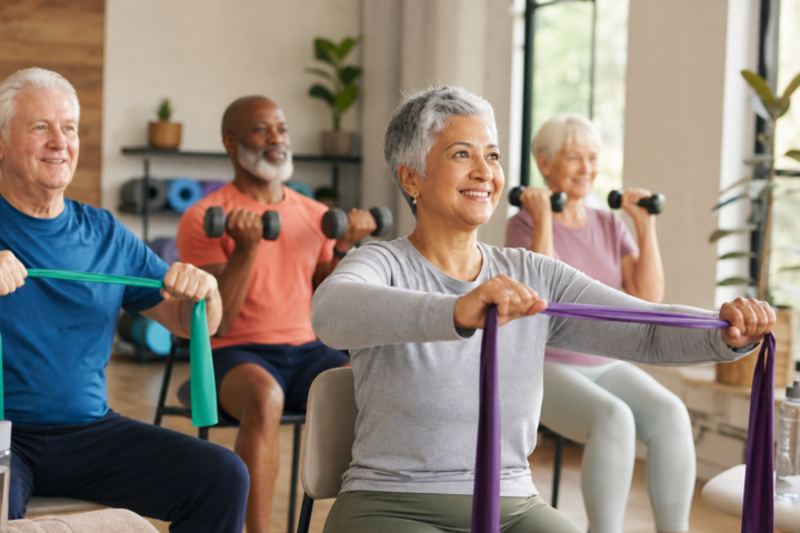 Older adults doing resistance band and dumbbell exercises in a bright room.