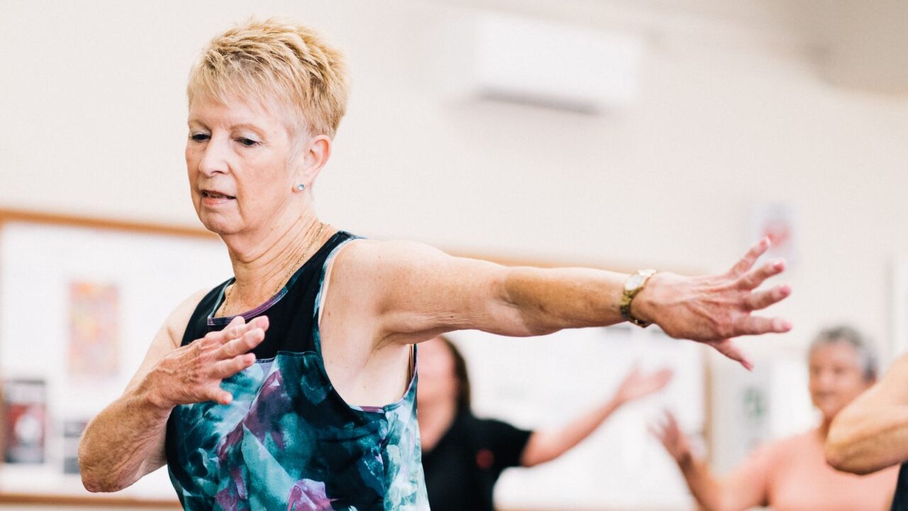 Woman over 60 practicing balance exercises in a group fitness class to prevent falls