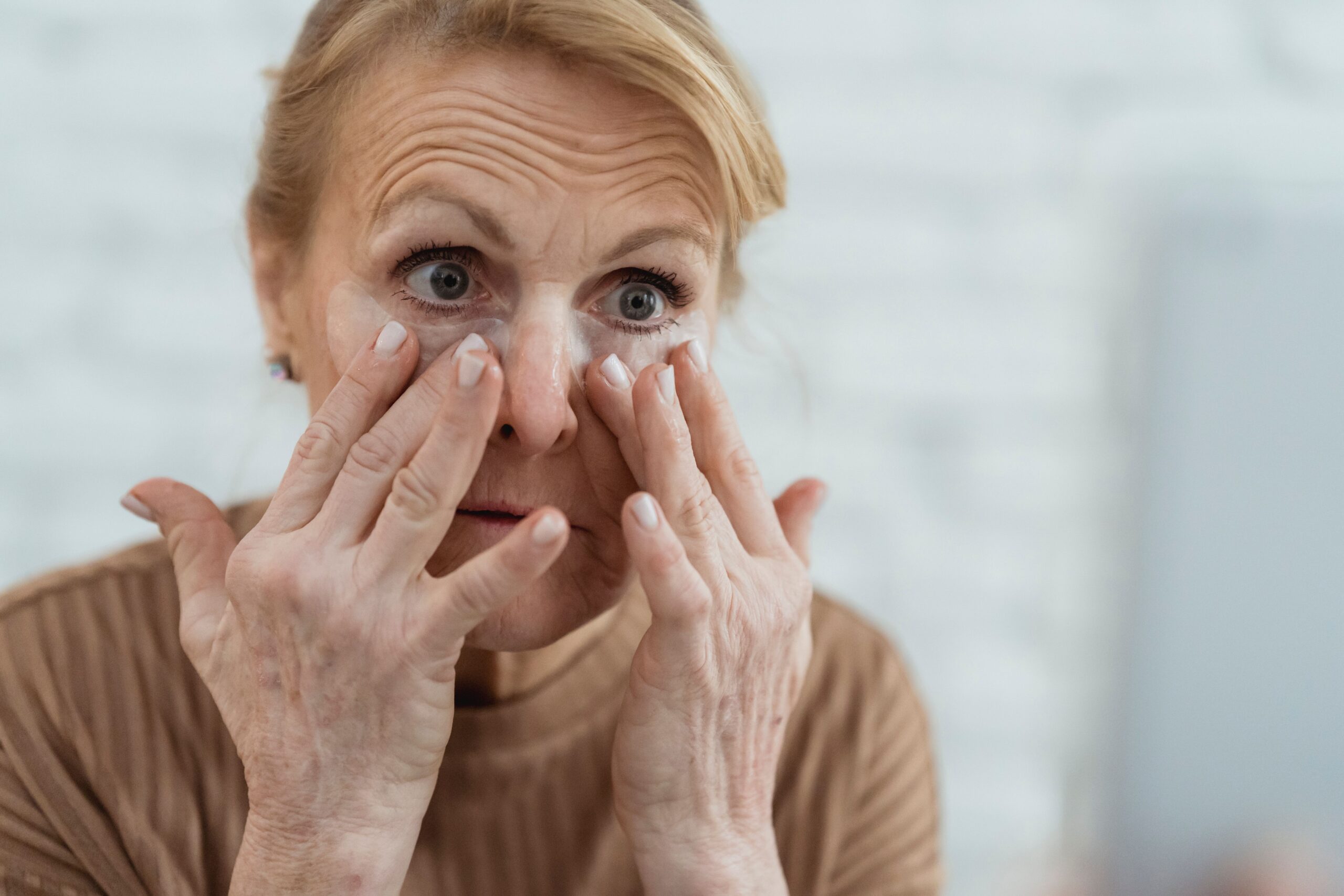 Mature woman applying eye cream as part of a skincare routine for aging skin