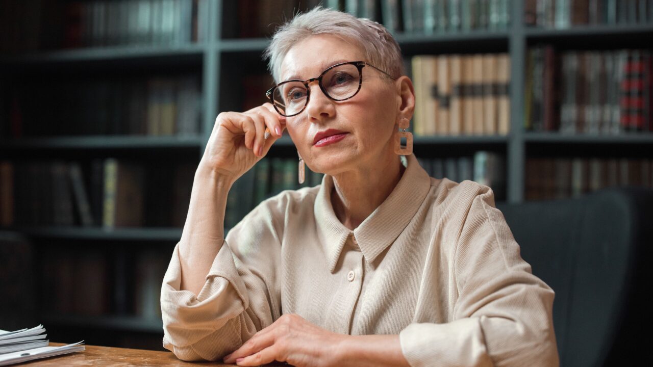 Thoughtful mature woman surrounded by books, representing cognitive health and aging