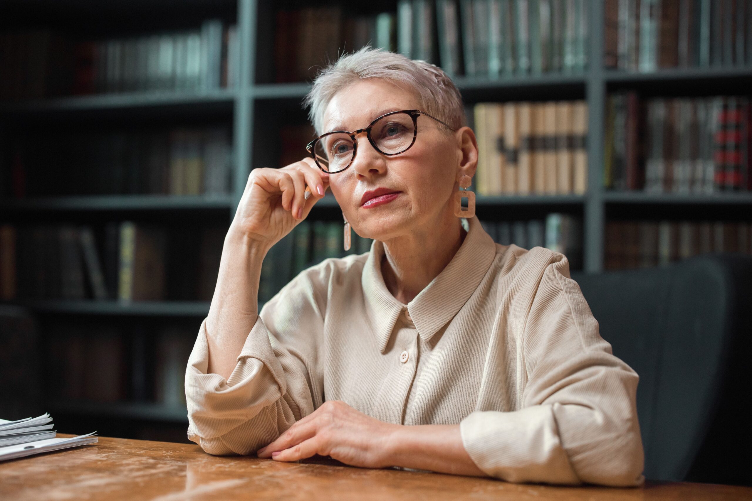 Thoughtful mature woman surrounded by books, representing cognitive health and aging